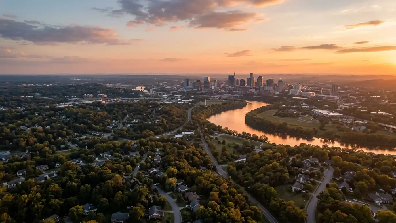 A golden sunset aerial view of the Nashville skyline above tree-covered suburban neighborhoods with a winding river